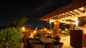 Un área de comedor al aire libre con mobiliario de mimbre y una pérgola de madera.