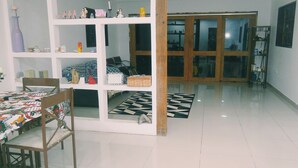 A room with a dining table, chairs, a white shelving unit with various items, a patterned rug, and a large wooden door.