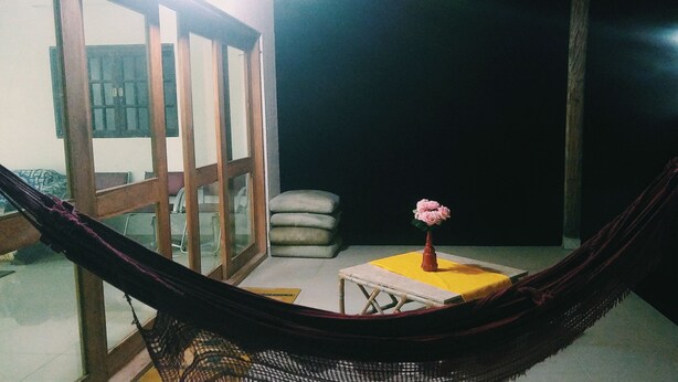 A hammock in a room with a small table and a vase of flowers.