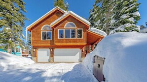Una casa de madera con dos puertas de garaje, rodeada de nieve y árboles.