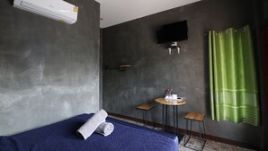 Una habitación con una cama, una mesita con artículos de aseo, un televisor montado en la pared y una cortina verde.
