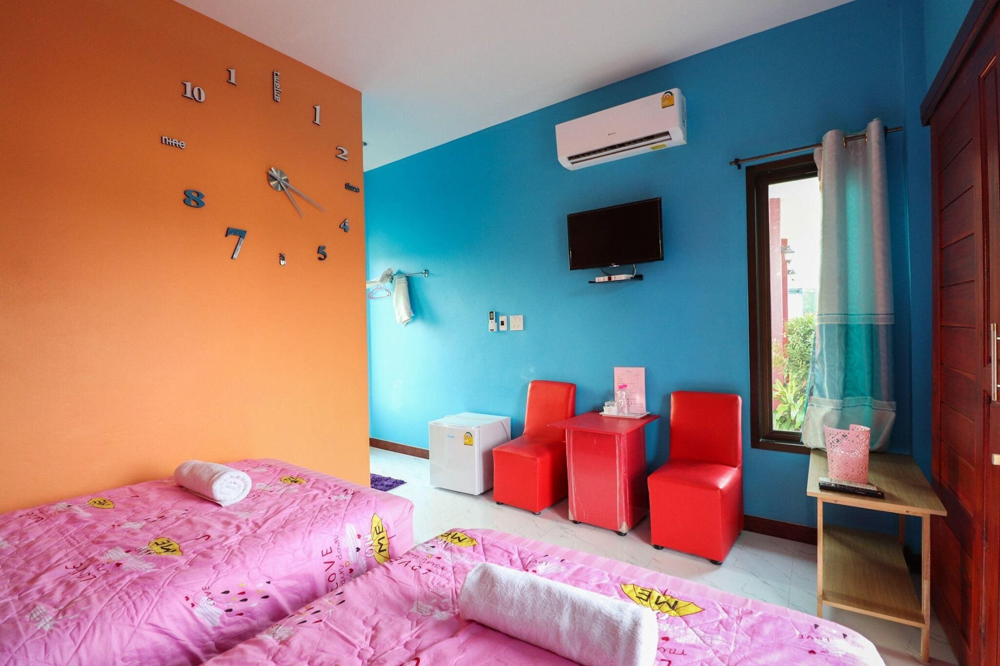 A bedroom with a bed, a TV, a window with curtains, and a wall clock.