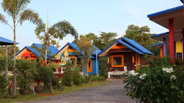 Una hilera de casas de campo coloridas con un camino de grava que las conduce, rodeadas de vegetación.