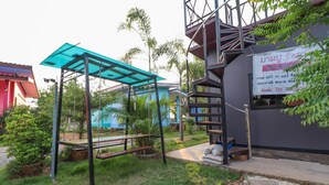 Un área de estar al aire libre techada con un conjunto de columpios, una escalera y un edificio que ofrece WiFi gratuito y un número de contacto.
