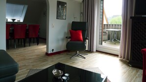 A modern living room with a dining area, a black leather chair with a red cushion, and a balcony with a view. - FeWo-Schuberski (Oerlinghausen)