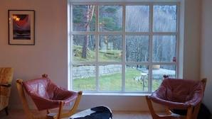 Una habitación con dos sillones de cuero, un tapete pequeño y un ventanal con vistas a un jardín y árboles.