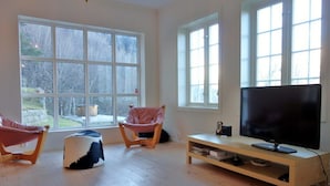 Una sala de estar con ventanas amplias, un televisor de pantalla plana y dos sillones.