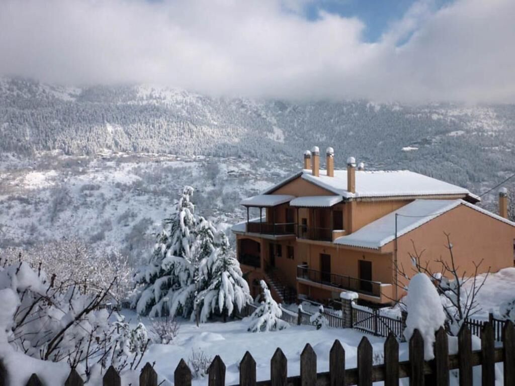 Un edificio de dos pisos con techo nevado y una valla de madera en primer plano.