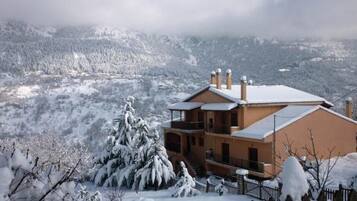 Un edificio de dos pisos con techo nevado y una valla de madera en primer plano.