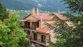 A two-story building with a red-tiled roof, balconies, and a mountainous backdrop.