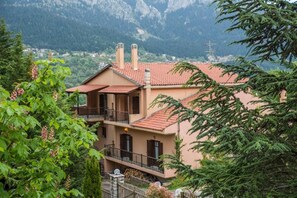 A two-story building with a red-tiled roof, balconies, and a mountainous backdrop. - Arhontiko Christodoulou (Prespes)