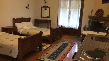 A bedroom with two wooden beds, a small table, a mirror, a window with curtains, and a fireplace.