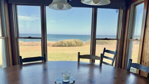 A table with two glasses of milk and decorative items, overlooking a grassy area with a view of the ocean. - Nauset Heights - The Ocean At Your Doorstep! (2127) (Orleans)