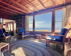 Een gezellige kamer met grote ramen, een houten plafond en een blauw vloerkleed.