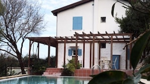 Vista a la piscina de una casa con una pérgola, un pequeño jardín y un cielo despejado.