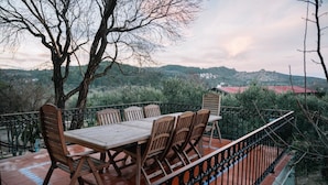 Una terraza con mesa y sillas de madera, rodeada por una verja de hierro forjado negro, con vistas a un paisaje montañoso.
