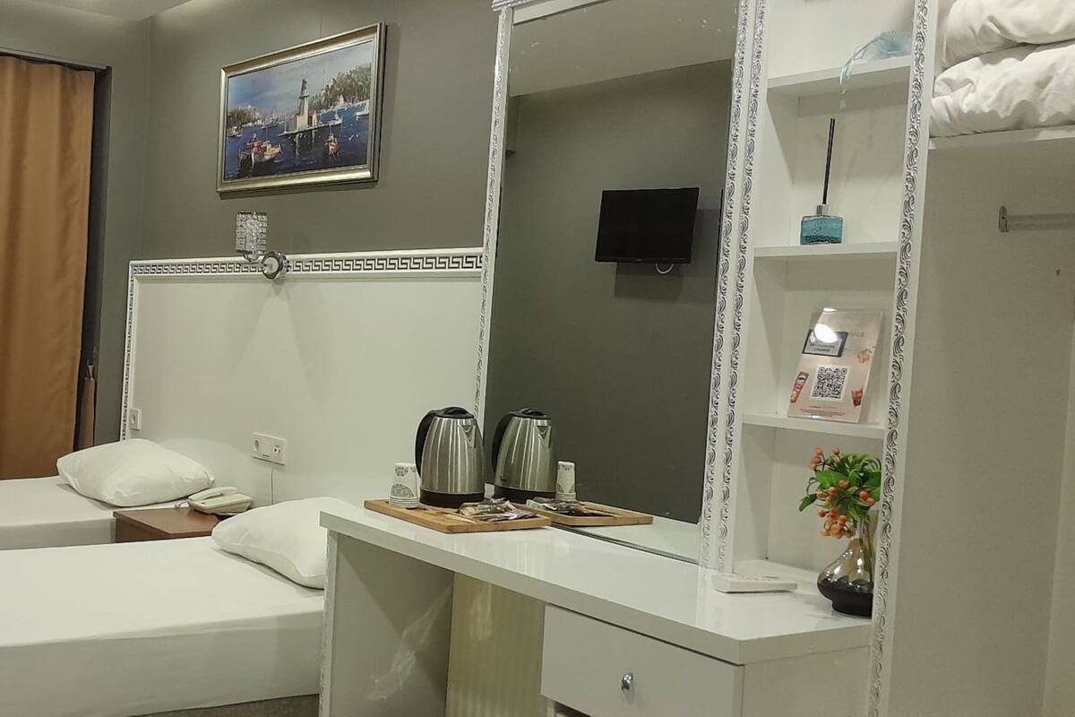A hotel room with two beds, a desk with a mirror, a TV, and a shelf with toiletries.