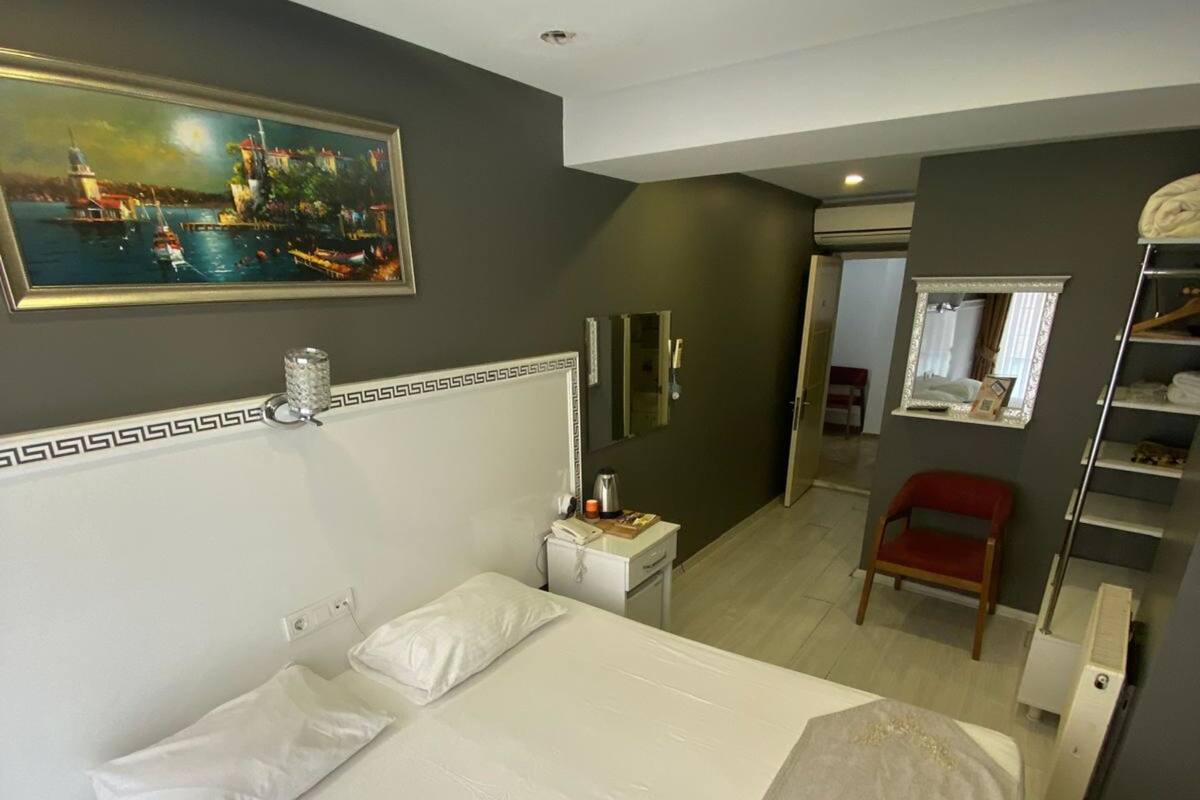 A hotel room with a large bed, a bedside table, a nightstand, a red chair, a mirror, and a painting on the wall.