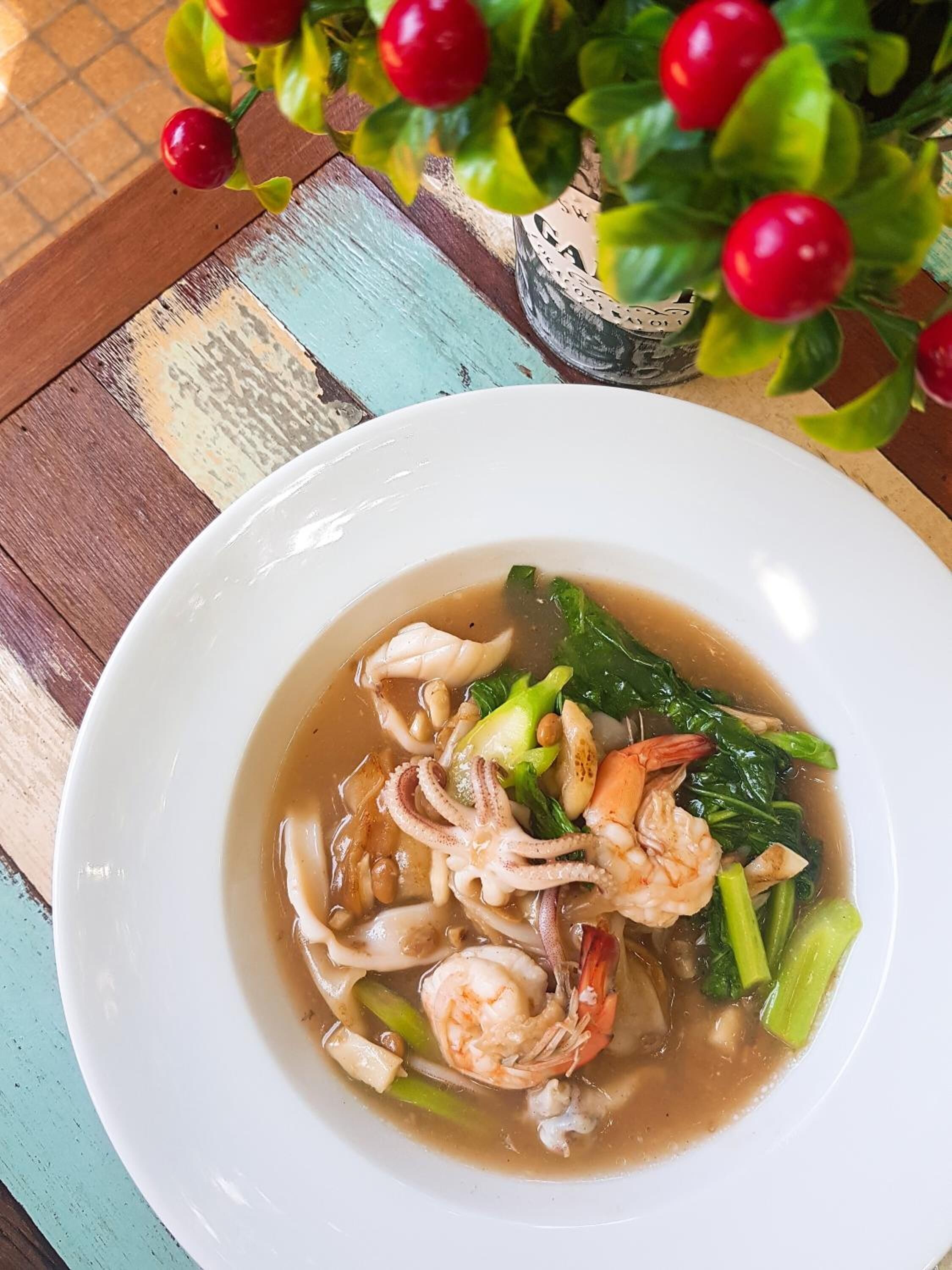 A bowl of soup with shrimp and vegetables on a table.