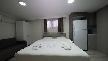 A hotel room with a bed, a sofa, a minibar, and a refrigerator.