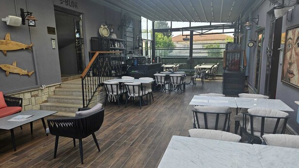 An indoor dining area with tables and chairs, a bar area with a counter, and a staircase leading to an upper level.