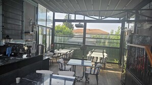 A modern kitchen with large windows, a dining area with tables and chairs, and a view of the neighborhood.