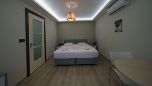 A modern bedroom with a skylight, a bed with a grey headboard, bedside tables with lamps, and a small table with a chair.