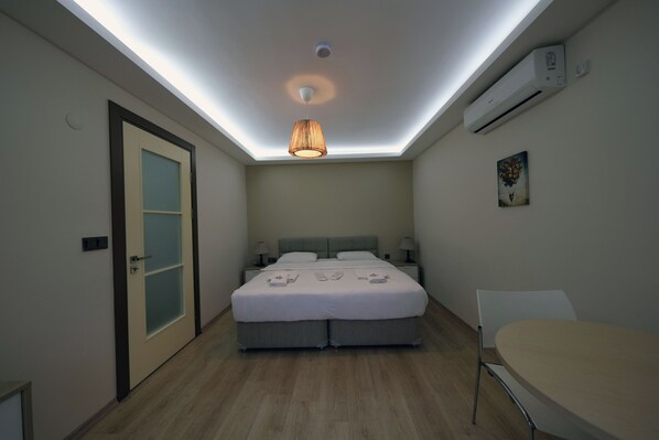 A modern bedroom with a skylight, a bed with a grey headboard, bedside tables with lamps, and a small table with a chair.