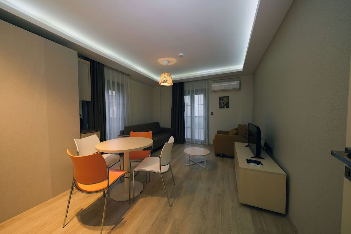 Un salon moderne avec une table de salle à manger ronde, des chaises orange, un canapé et un téléviseur posé sur un meuble.