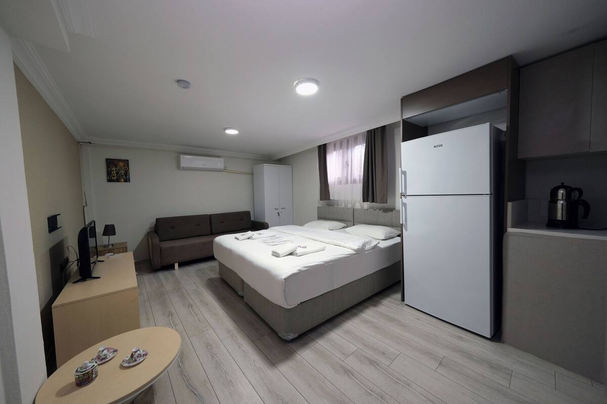 Une chambre d’hôtel équipée d’un lit, d’un bureau, d’une kitchenette et d’une petite table avec des chaussons.