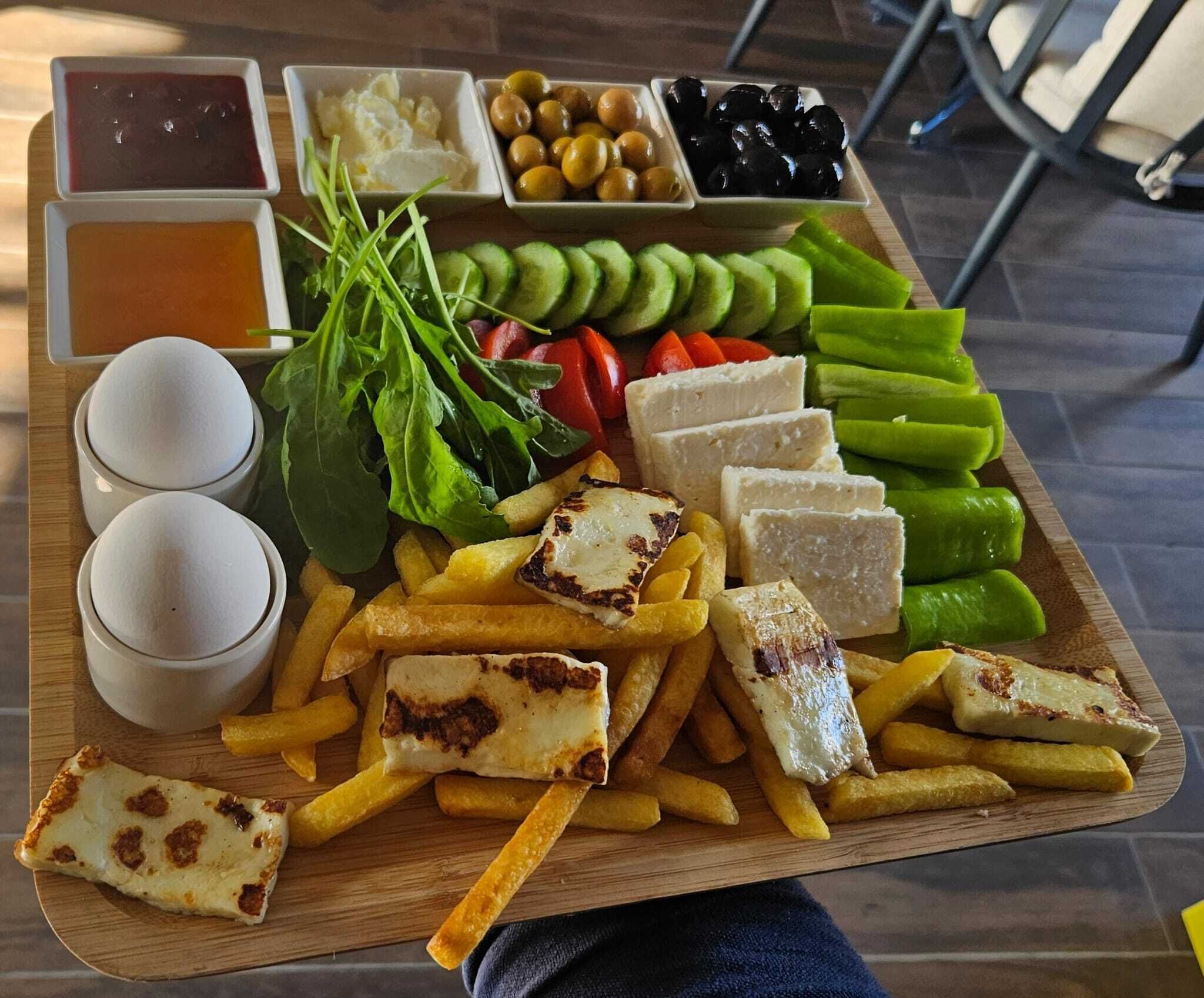 Una tabla de madera con diversos alimentos, como queso, papas fritas y verduras, junto con recipientes pequeños de salsas.