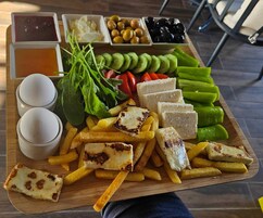 Una tabla de madera con diversos alimentos, como queso, papas fritas y verduras, junto con recipientes pequeños de salsas.
