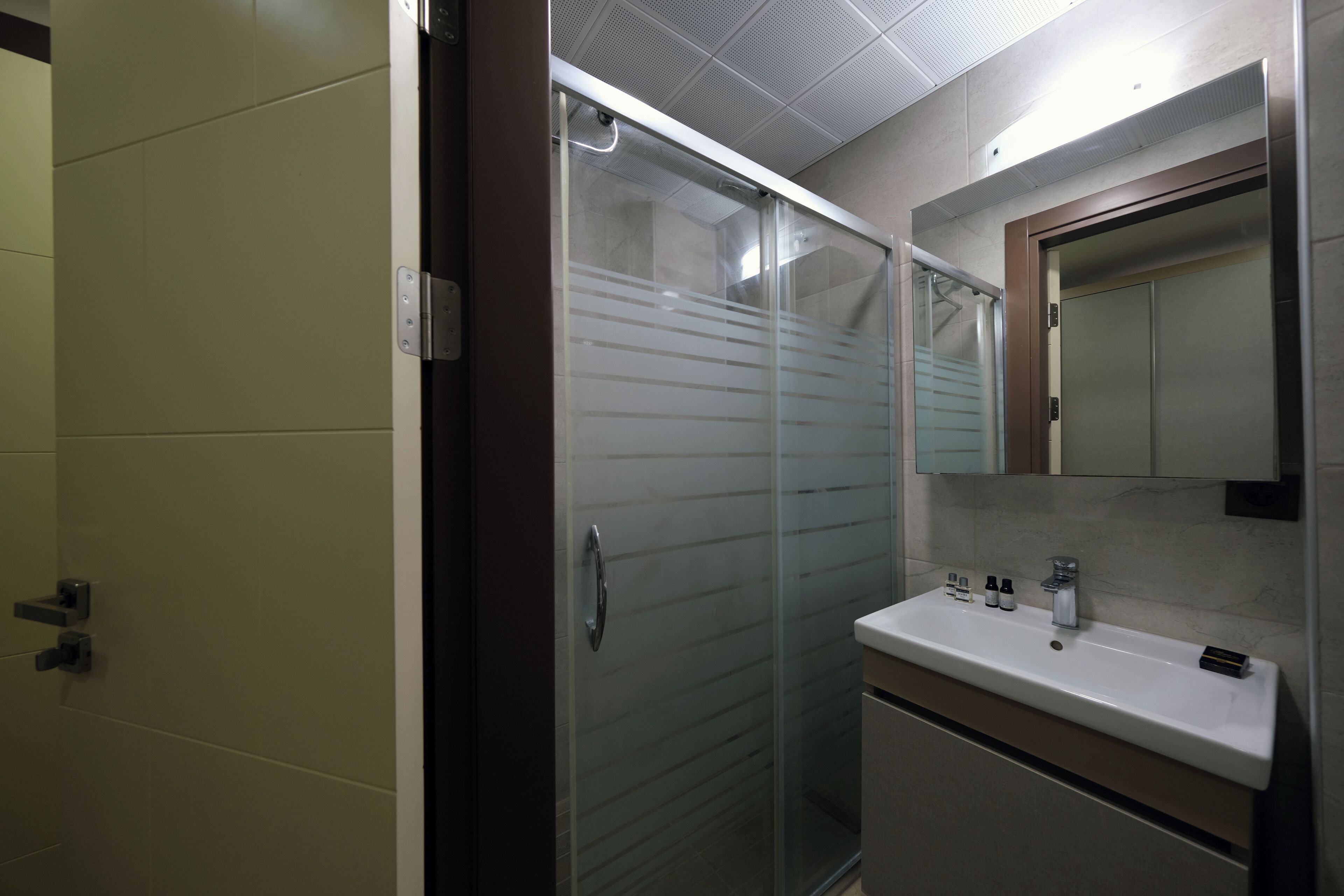 A modern bathroom with a glass shower enclosure, a white sink with a mirror above it, and a beige vanity.
