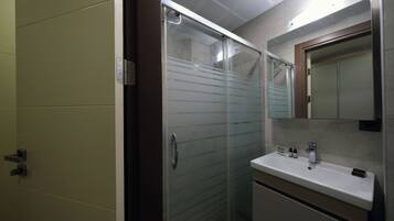 A modern bathroom with a glass shower enclosure, a white sink with a mirror above it, and a beige vanity.
