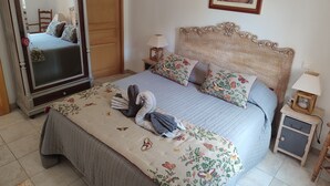Une chambre avec un grand miroir, un lit recouvert d’une literie à motifs floraux, une tête de lit en bois, une table de chevet avec une lampe et une œuvre d’art encadrée accrochée au mur.