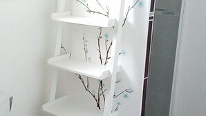 Une salle de bain avec des toilettes blanches, une étagère blanche ornée de branches et de fleurs, et une cabine de douche en verre.