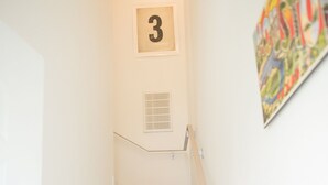 Eine Treppe mit einem Hinweisschild mit der Nummer 3, weißen Wänden und einem farbenfrohen Kunstwerk auf der rechten Seite.