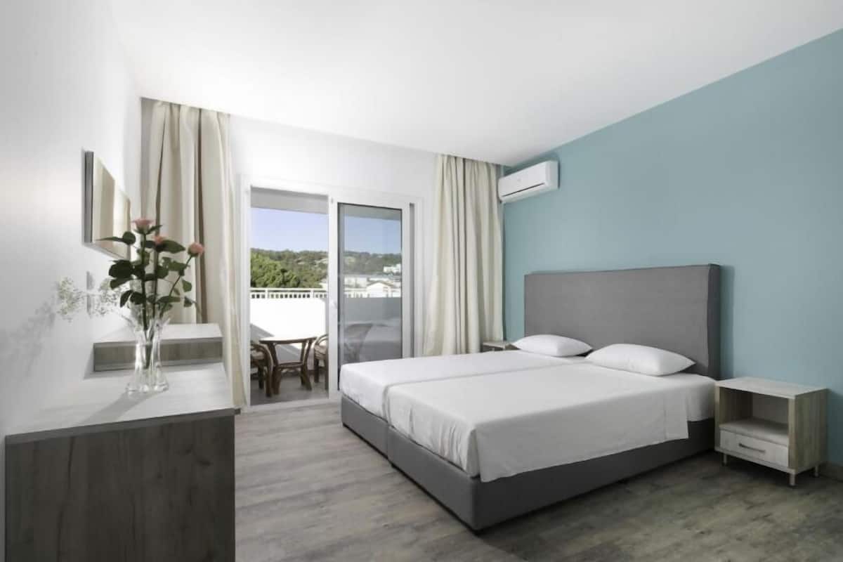 Una habitación de hotel moderna con una cama grande, una mesita de noche, un florero con flores y vistas al exterior.