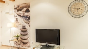 Ein modernes Wohnzimmer mit Flachbildfernseher auf einem Glastisch, einer Wanduhr und einem gerahmten Bild.