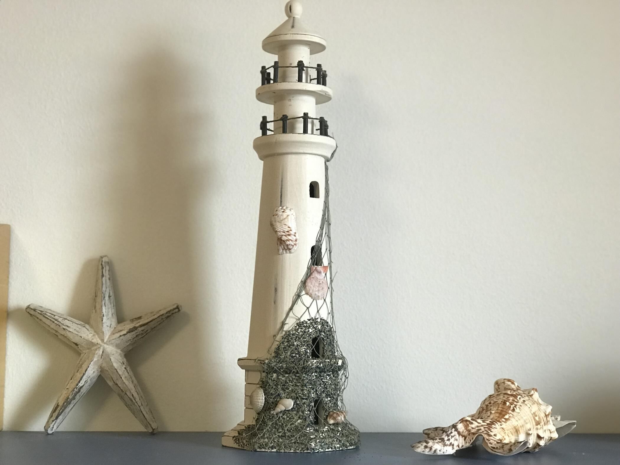 Un modelo de faro con escalera en espiral, una estrella de mar y conchas marinas.