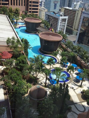 A rooftop pool area with multiple swimming pools, palm trees, and a large building labeled "MENARA" in the background. - Times Square Residence At Kuala Lumpur (Kuala Lumpur)