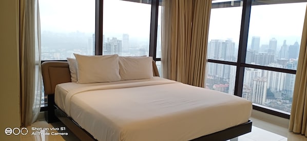 A modern bedroom with a large bed, a view of a cityscape through floor-to-ceiling windows, and a city view from the window. - Times Square Residence At Kuala Lumpur (Kuala Lumpur)