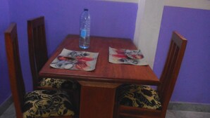 A dining table with four chairs, a bottle of water, and placemats with a floral design. - Kimis Place (Douala)