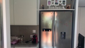 Eine kompakte Küche mit einem Edelstahlkühlschrank, einer kleinen Arbeitsfläche und einem an der Wand befestigten Regal mit Fotos.