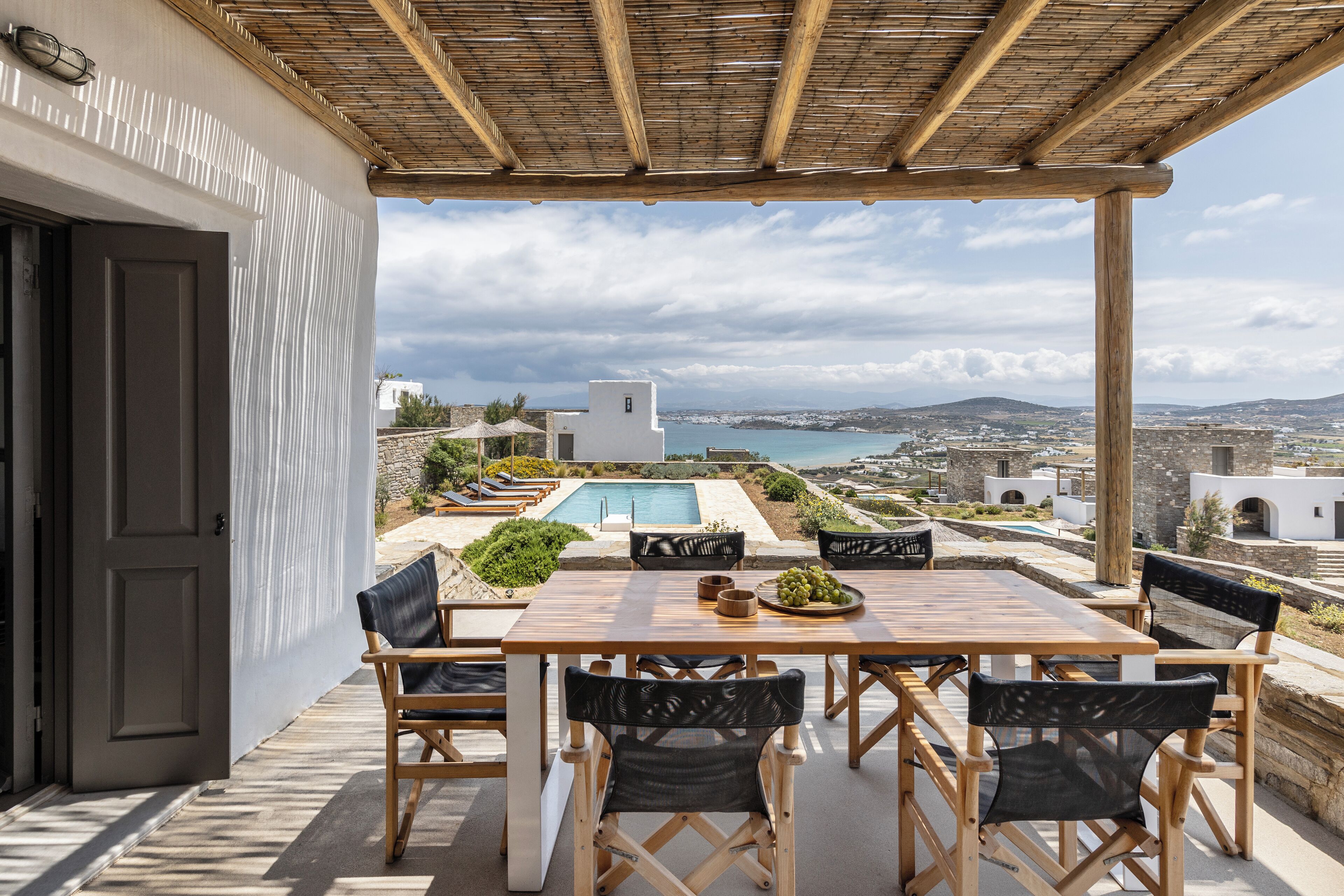 Eine Außenpatio mit Holztisch und -stühlen, einem Pool und Blick auf das Meer und die Hügellandschaft.