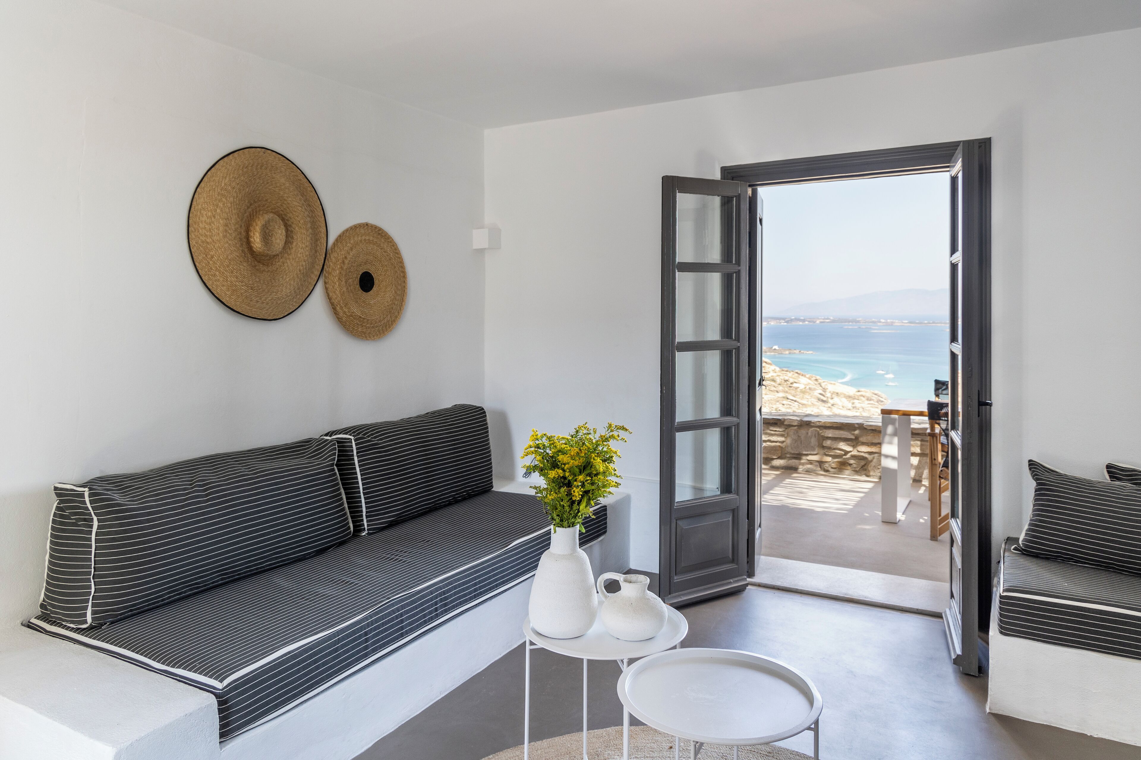 Un salon moderne avec un canapé, une petite table et une vue sur la plage, visible à travers une porte ouverte.