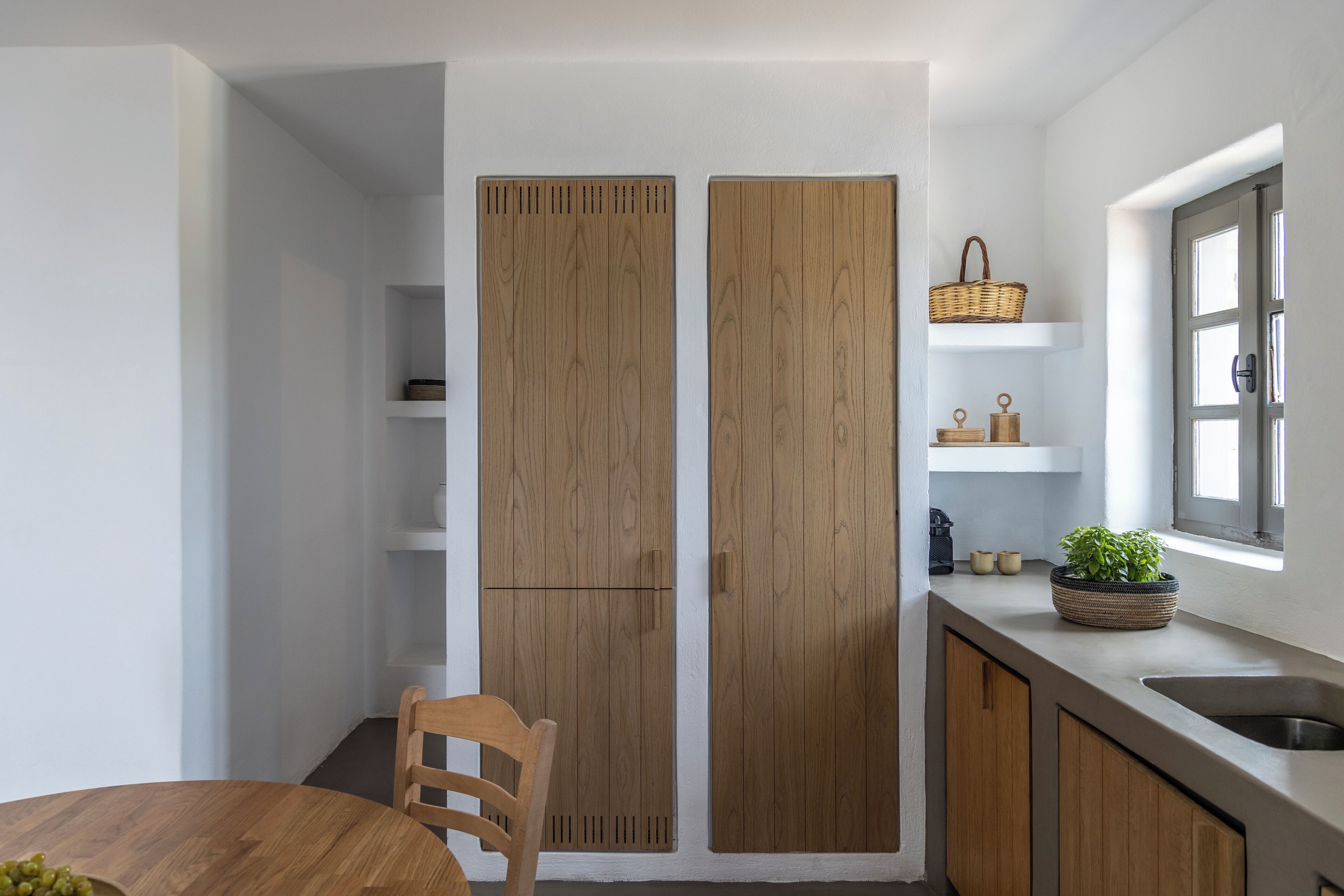 A kitchen with wooden cabinets, a dining table with chairs, and a window with a basket on the counter.