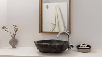 A bathroom with a wooden-framed mirror, a dark stone sink, and a small vase with dried flowers on the countertop.