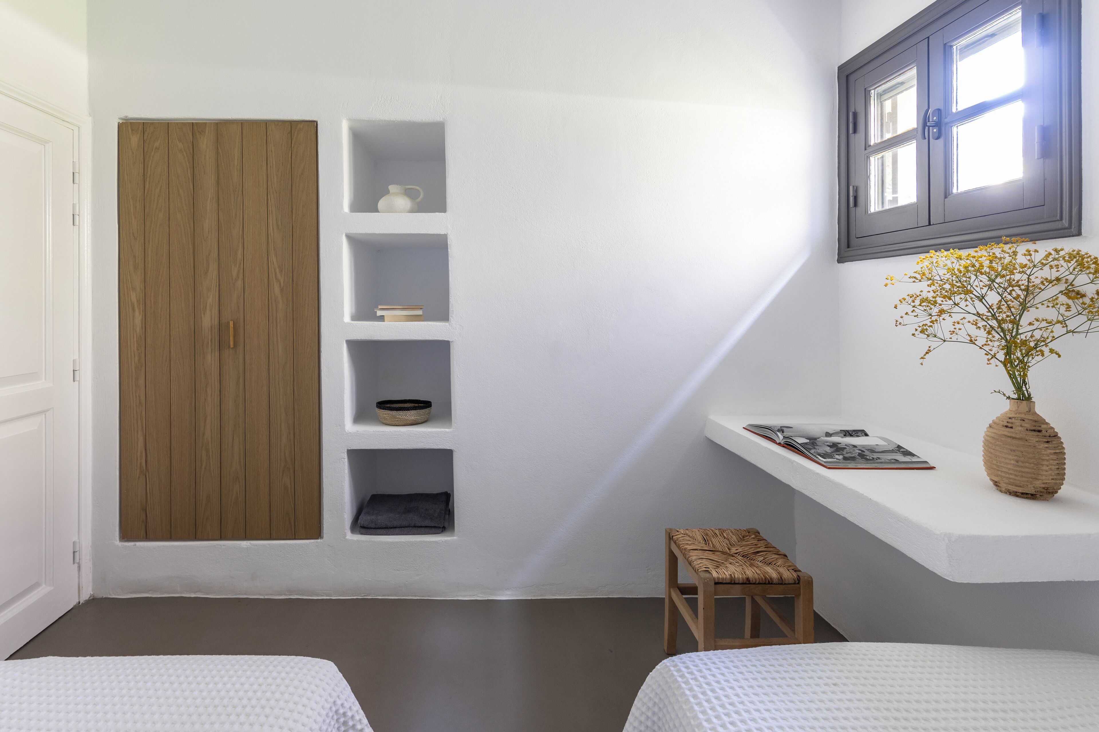 Une chambre avec une armoire en bois, des étagères intégrées, un petit tabouret et une fenêtre donnant sur un beau paysage.