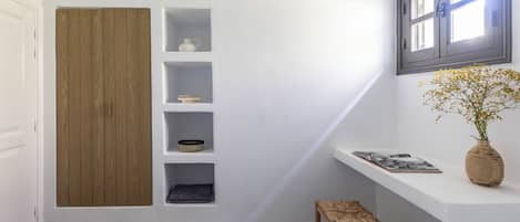 Une chambre avec une armoire en bois, des étagères intégrées, un petit tabouret et une fenêtre donnant sur un beau paysage.